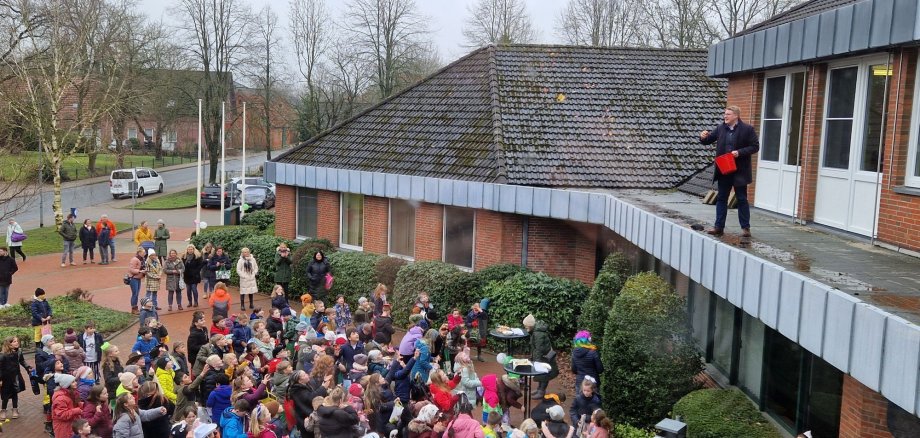 Bürgermeister Henrik Wärner wirft Bonbons vom Vordach für die Schüler der Grundschule Schiffdorf